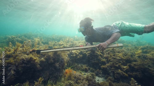 Underwater shot of a spearfisher man holding a speargun and swimming underwater. photo