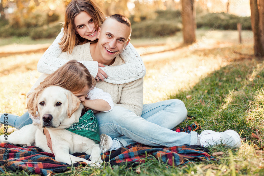 Fototapeta premium Happy beautiful family with dog labrador is having fun are sitting on green grass in park.