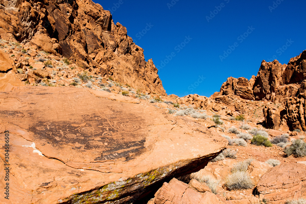 Wide-angle view of pre-Columbian petroglyphs on a large rock in a canyon in Valley of Fire State Park in Nevada