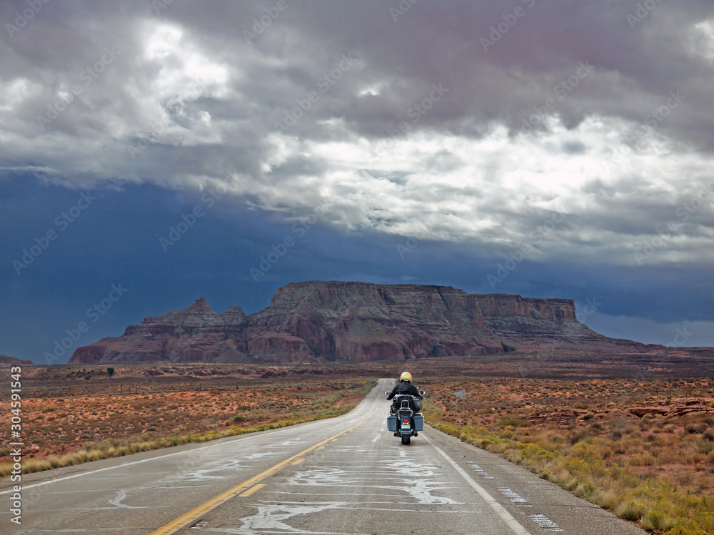 Fototapeta premium Biker riding on lonely Arizona desert road, red rocks ahead