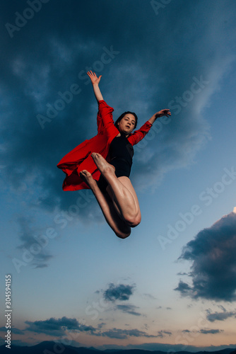 Flexible young woman in ballet figure against blue sky