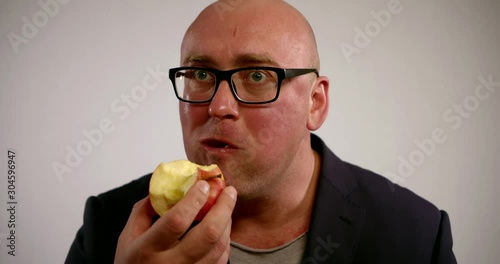 a large bald man in glasses and a dark jacket holds a bunch of lettuce in his hand. he grudgingly bites and chews. white background photo
