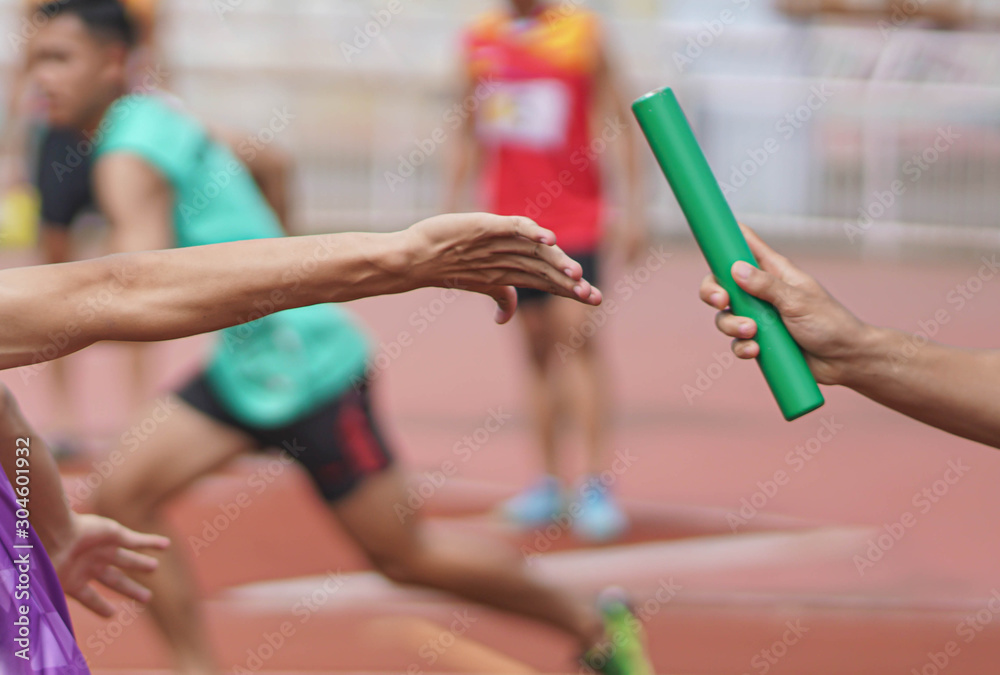 Obraz premium Professional Athlete passing a baton to the partner against race on racetrack.selective focus.