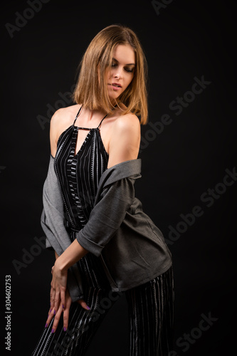 Young beautiful woman wearing in black overalls and cardigan  posing over black background, top view. Studio shot of  brunette woman against isolated background