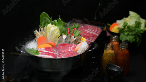 Close-up view of shabu shabu in hot pot with black background, fresh sliced meat, sea food and vegetables