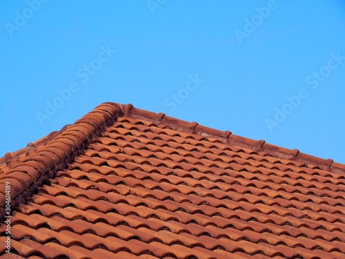 Roof covered with orange wavy tiles with blue sky background.