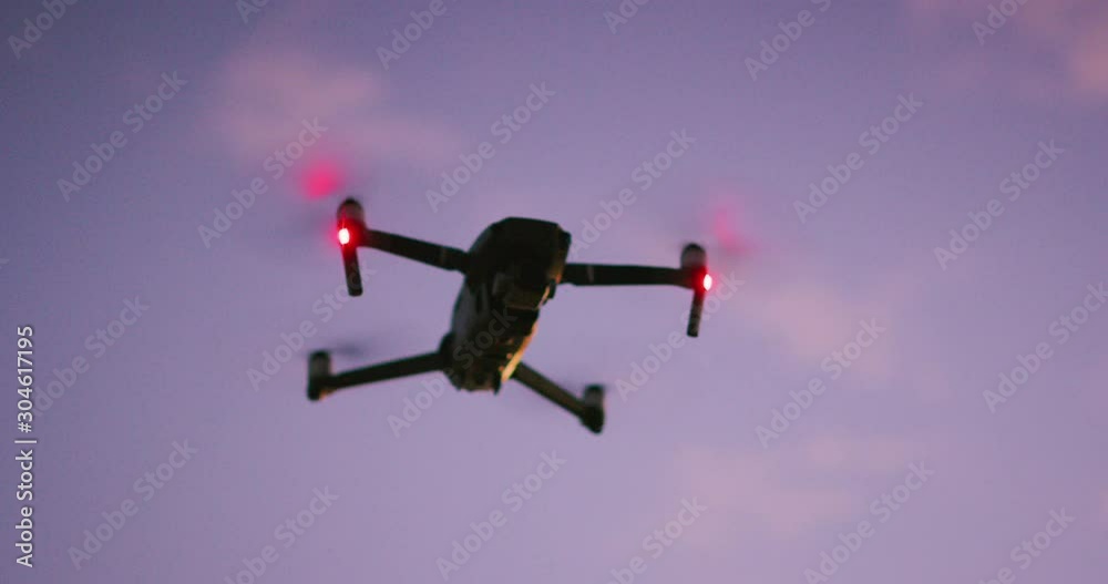 A silhouette of UAV drone flying with red signal lights in the sky at dusk with purple pink clouds