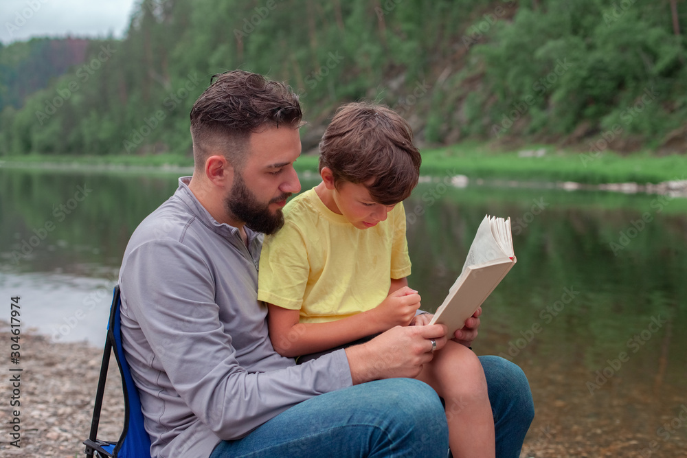 A man with a boy in nature are reading a book. family and fatherhood concept