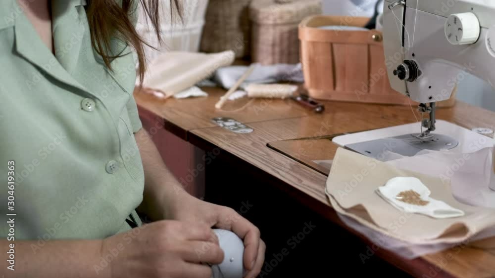 The tailor is sewing a toy. The woman is in the garment factory. The table is wooden. The tailor is sewing a toy. The woman is in the garment factory. The table is wooden.