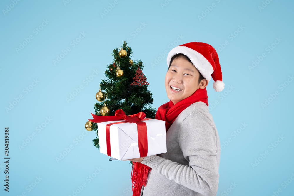 Happy Asian preteen boy holding Christmas tree and gift box on blue background, Christmas concept. Happy Asian preteen boy holding Christmas tree and gift box on blue background, Christmas concept.