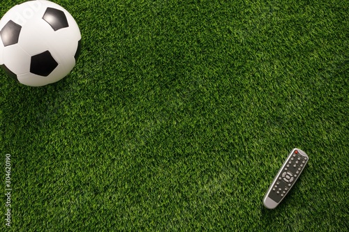 Soccer ball on a green field and a TV remote control. Flat lay concept of football matches. Copy space.
