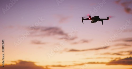 Orbiting view of a quadcopter drone silhouette hovering and flying at sunset with a purple yellow sky
