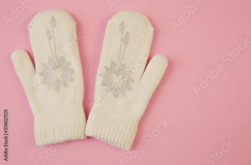 White wool mittens with rhinestone snowflake isolated on a pink background with copy space. flat lay, top view. The concept of winter clothing and accessories Winter background, banner, pattern, card.