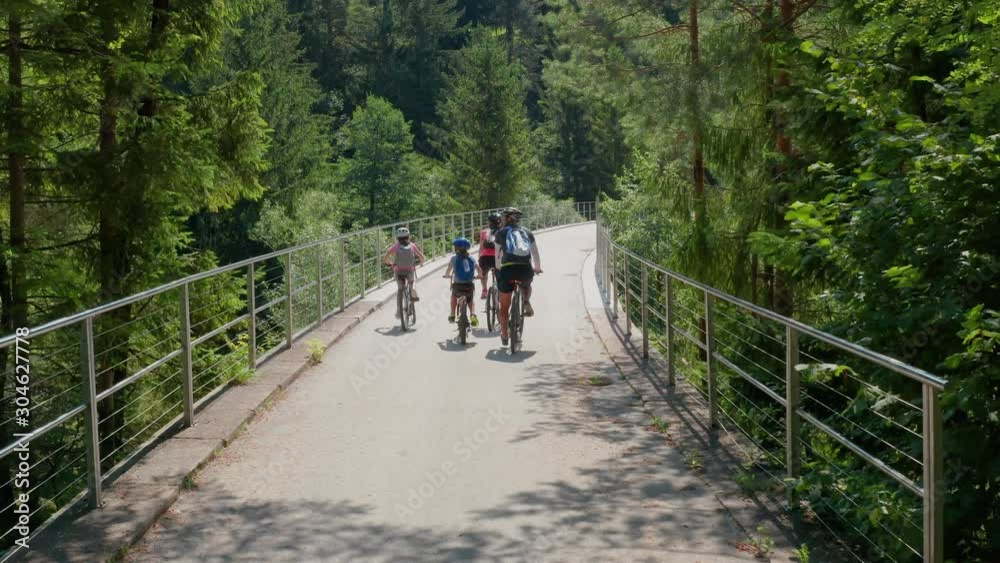 Dolly shot Caucasian family parents and children in bicycles crossing a bridge together in Slovenia, Drone follows them closely behind Dolly shot Caucasian family parents and children in bicycles crossing a bridge together in Slovenia, Drone follows them closely behind