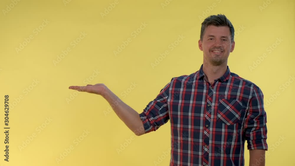 Handsome man presenting something on empty hand with yellow background. He looking on copy space for product. Handsome man presenting something on empty hand with yellow background. He looking on copy space for product.
