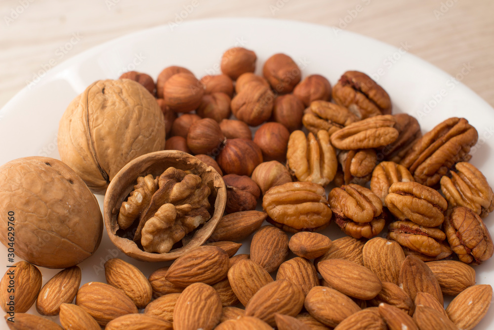 walnuts, almonds, pecans and hazelnuts on a white plate on a woodden table