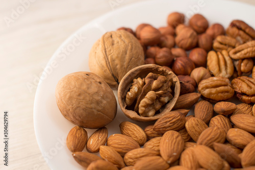 walnuts, almonds, pecans and hazelnuts on a white plate on a woodden table