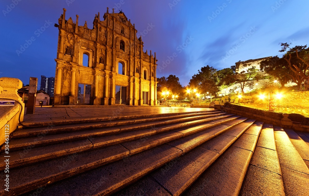 Scenery of the Ruins of St. Paul's Church in the Historic Center of Macau, China, with a stairway leading to the beautiful facade of the historical architecture & lights glistening in morning twilight
