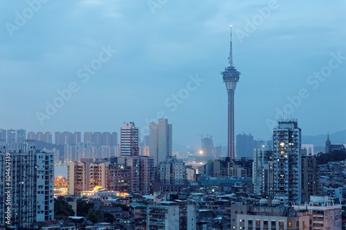 Urban skyline of vibrant Macao City in blue evening twilight, with the famous landmark Macau Tower (Convention & Entertainment Center) and hotels & casinos among crowded buildings at dusk
