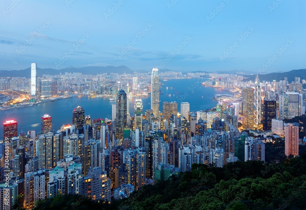 Night scenery of Hong Kong viewed from top of Victoria Peak with city skyline of crowded skyscrapers by Victoria Harbour & Kowloon area across the busy seaport ~ Cityscape of Hongkong in blue twilight