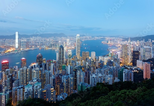 Night scenery of Hong Kong viewed from top of Victoria Peak with city skyline of crowded skyscrapers by Victoria Harbour   Kowloon area across the busy seaport   Cityscape of Hongkong in blue twilight