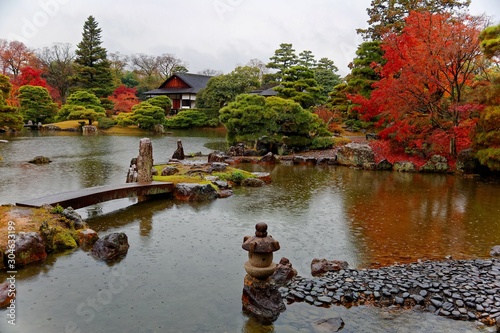 Autumn scenery of a beautiful Japanese garden in a public park in Kyoto, Japan, with view of fiery maple trees by the lake and a stone bridge over the pond on a rainy day photo