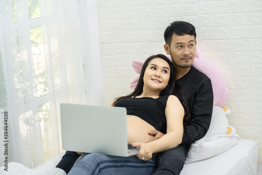 A beautiful pregnant woman and her handsome husband are smiling while spending time together in bed. A man is listening to the sound of a baby in his stomach. A beautiful pregnant woman and her handsome husband are smiling while spending time together in bed. A man is listening to the sound of a baby in his stomach.