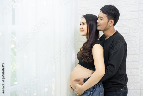 His beautiful boyfriend and pregnant wife were hugging and smiling while standing near the window at home.