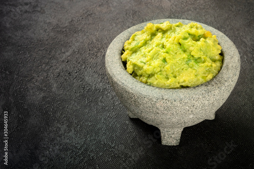 Guacamole in a molcajete, Mexican avocado dip sauce in the traditional stone mortar, on a black background with copy space