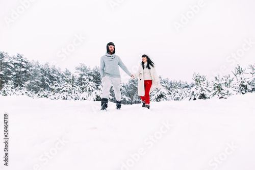 A girl and a guy walk in a snowy winter forest and have fun