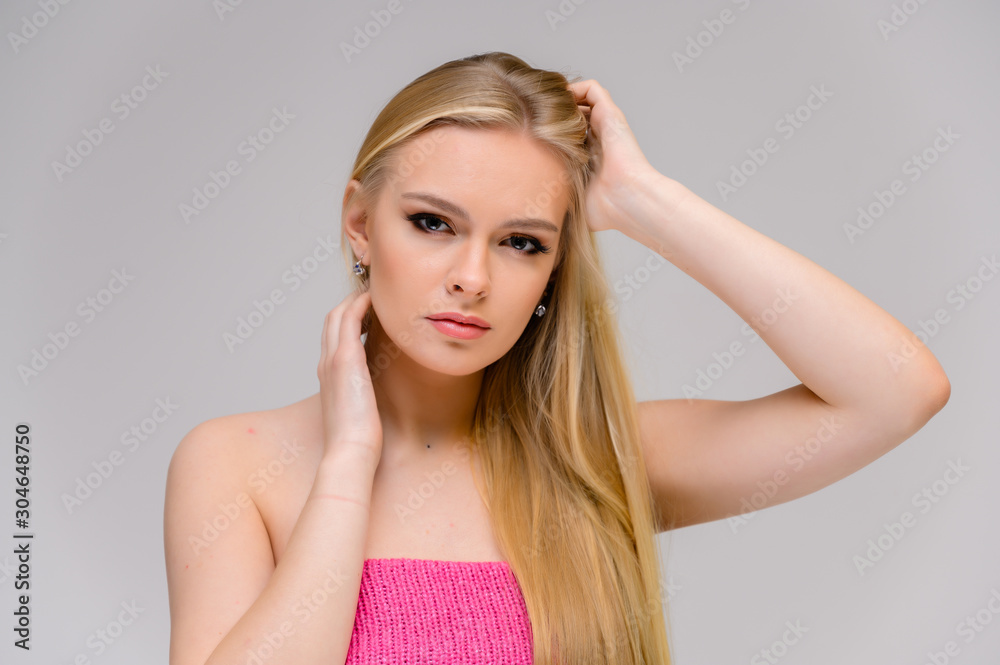 Fototapeta premium Beauty concept is a pretty model right in front of the camera. Close-up portrait of a beautiful blonde girl with excellent makeup with long smooth hair on a white background.