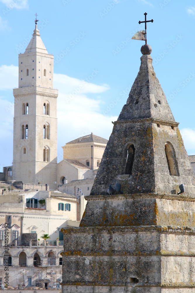 Point of two bell towers and church in the ancient city of Matera in Italy. Construction with blocks of tufa stone. Chileo blue with clouds.