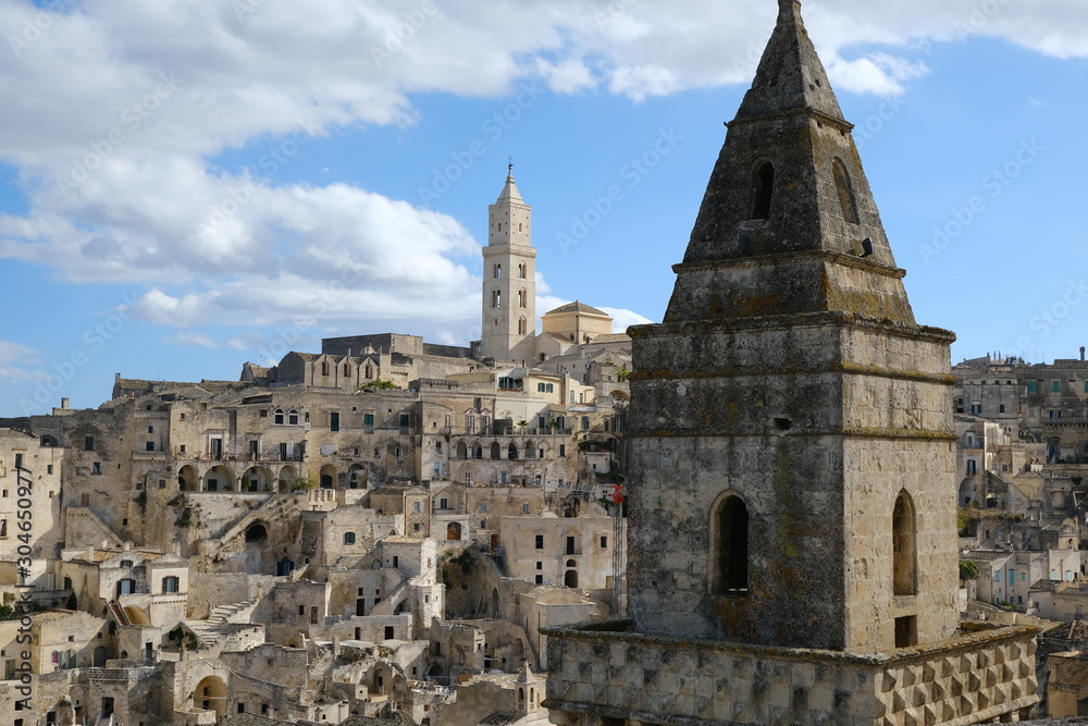 Point of two bell towers and church in the ancient city of Matera in Italy. Construction with blocks of tufa stone. Chileo blue with clouds.