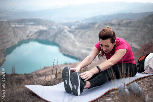 40s years woman dressed sportswear, pink topic and black fitness leggings, doing streching sport exercise outdoor against the heart shaped quarry .