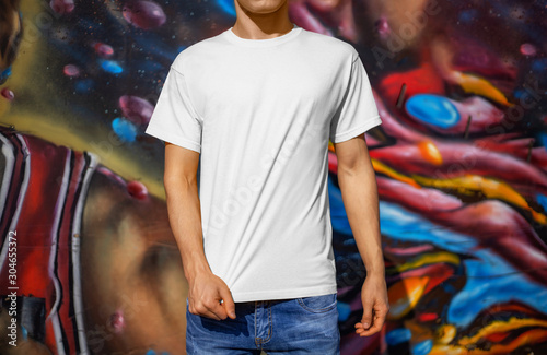 Mockup of a white T-shirt on a young guy against the background of a colorful wall, outdoors, front view.
