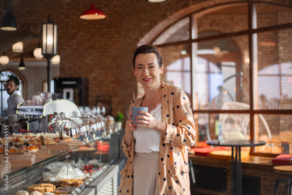 Matured middle aged woman dressed style fasnion clothes chooses the pastry bakery on showcase table in cafe.