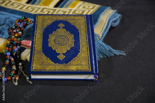 Closuep of Muslims Holy book Quran with a Colorful Tasbeeh Paternoster and Prayer rug Janamaz on black background 