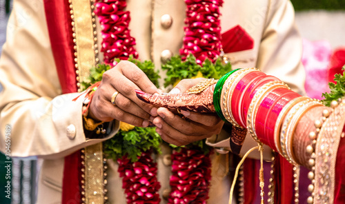 Engagement Ring ceremony- Indian Hindu male putting ring on bride's decorated finger. Couple is well attired as per traditional Indian Hindu wedding. Groom wearing Jodhpuri suit and floral garland.