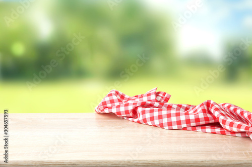 Red checkered picnic cloth on wooden table empty space background.