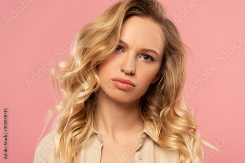 Displeased blonde woman looking at camera isolated on pink