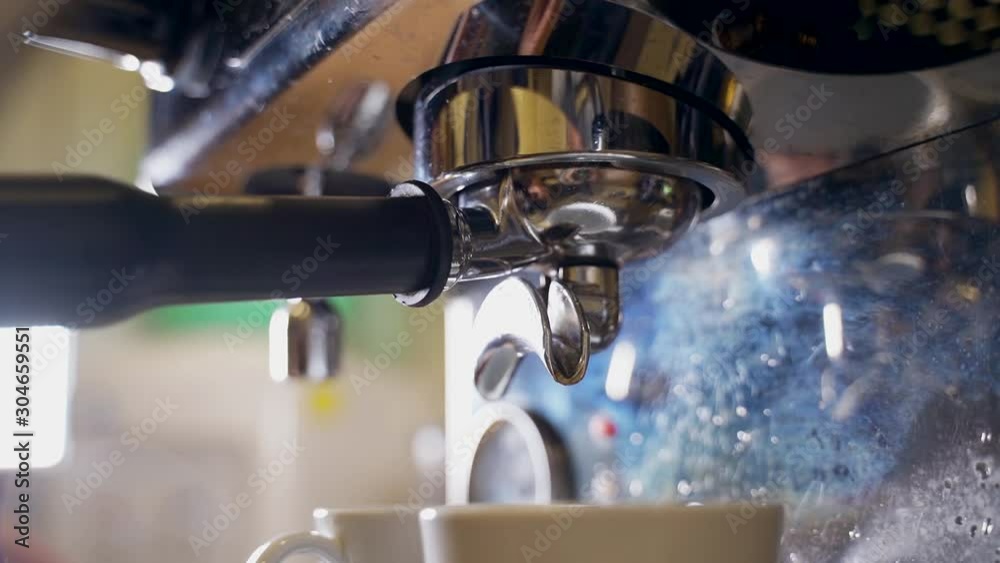 Pouring coffee stream from professional machine in cup. Barista man making double espresso, using filter holder. Flowing fresh ground coffee.