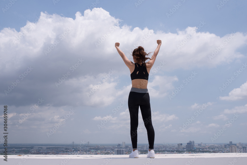 Rear view of beautiful woman in stylish sportswear standing on the rooftop. After the workout Rear view of beautiful woman in stylish sportswear standing on the rooftop. After the workout