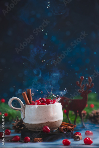 Cranberry winter drink with water drops, cinnamon, steam, and a wooden decorative deer.