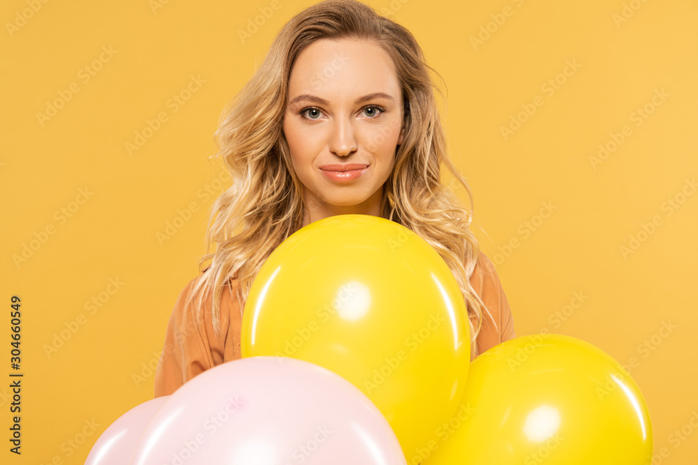 Smiling blonde woman holding balloons isolated on yellow Smiling blonde woman holding balloons isolated on yellow