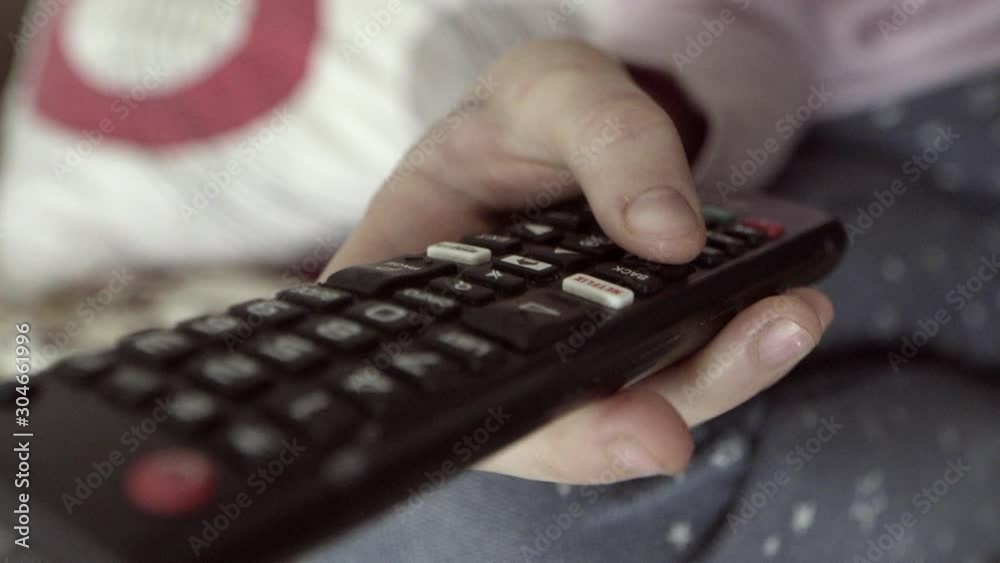 TV remote control close-up. Change channels on the TV remote. Children's hand using a TV remote control TV remote control close-up. Change channels on the TV remote. Children's hand using a TV remote control