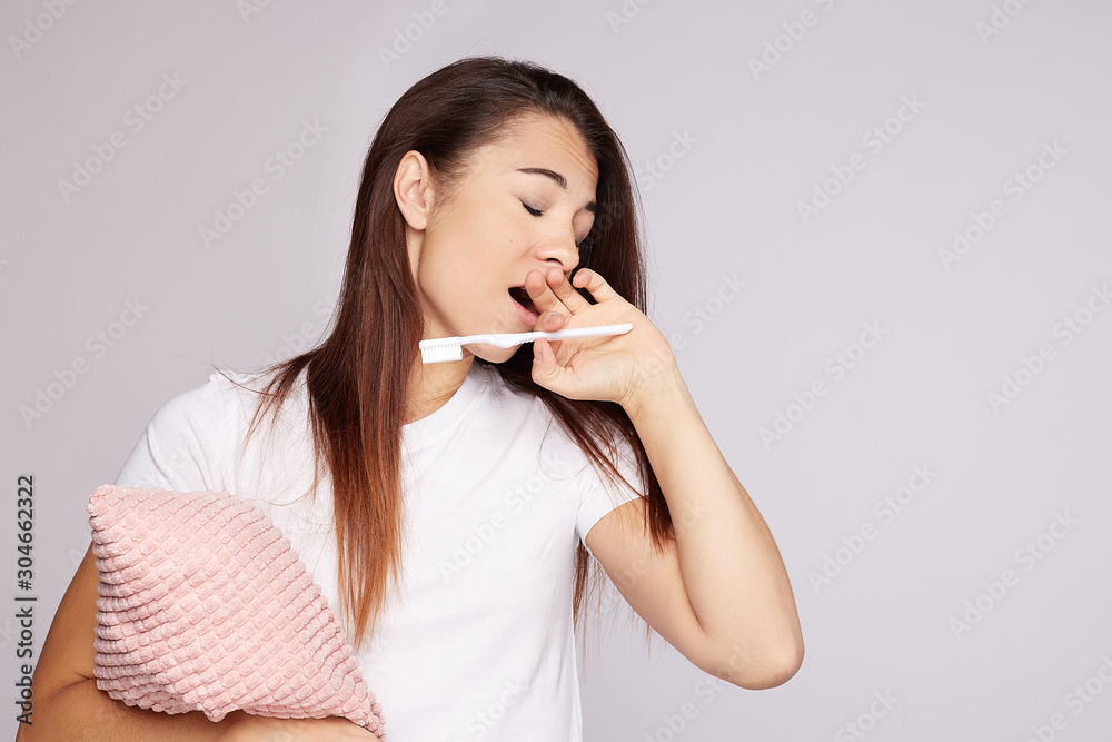 Close-up portrait of sleepy housewife covering mouth with hang while yawning being tired after sleepless night. Young pretty mother of newborn baby looks exhausted after hard night, holding pillow. Close-up portrait of sleepy housewife covering mouth with hang while yawning being tired after sleepless night. Young pretty mother of newborn baby looks exhausted after hard night, holding pillow.