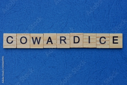 word cowardice made from brown wooden letters lies on a blue table 