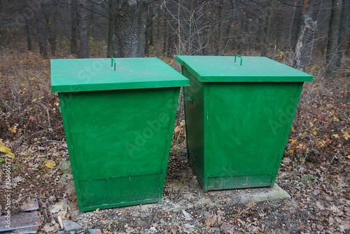 two green iron garbage cans stand in nature in autumn park