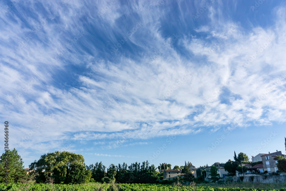 Small wave of beautiful white fluffy clouds on vivid blue sky in a summer time above houses and green trees in Vacqueyras village of wine, southeastern France