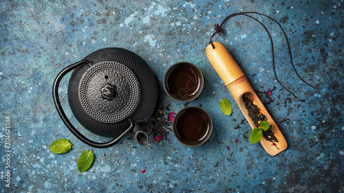 Black japanese cast iron teapot and dry tea in bamboo scoop with mint